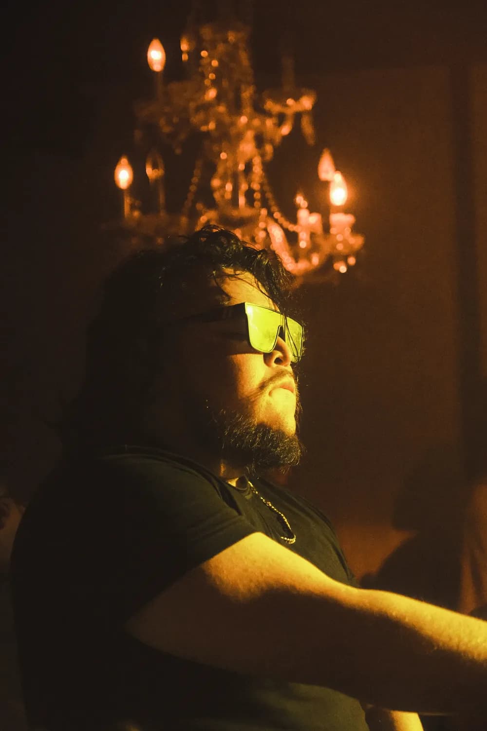 Papi AQ in amber light under a chandelier.