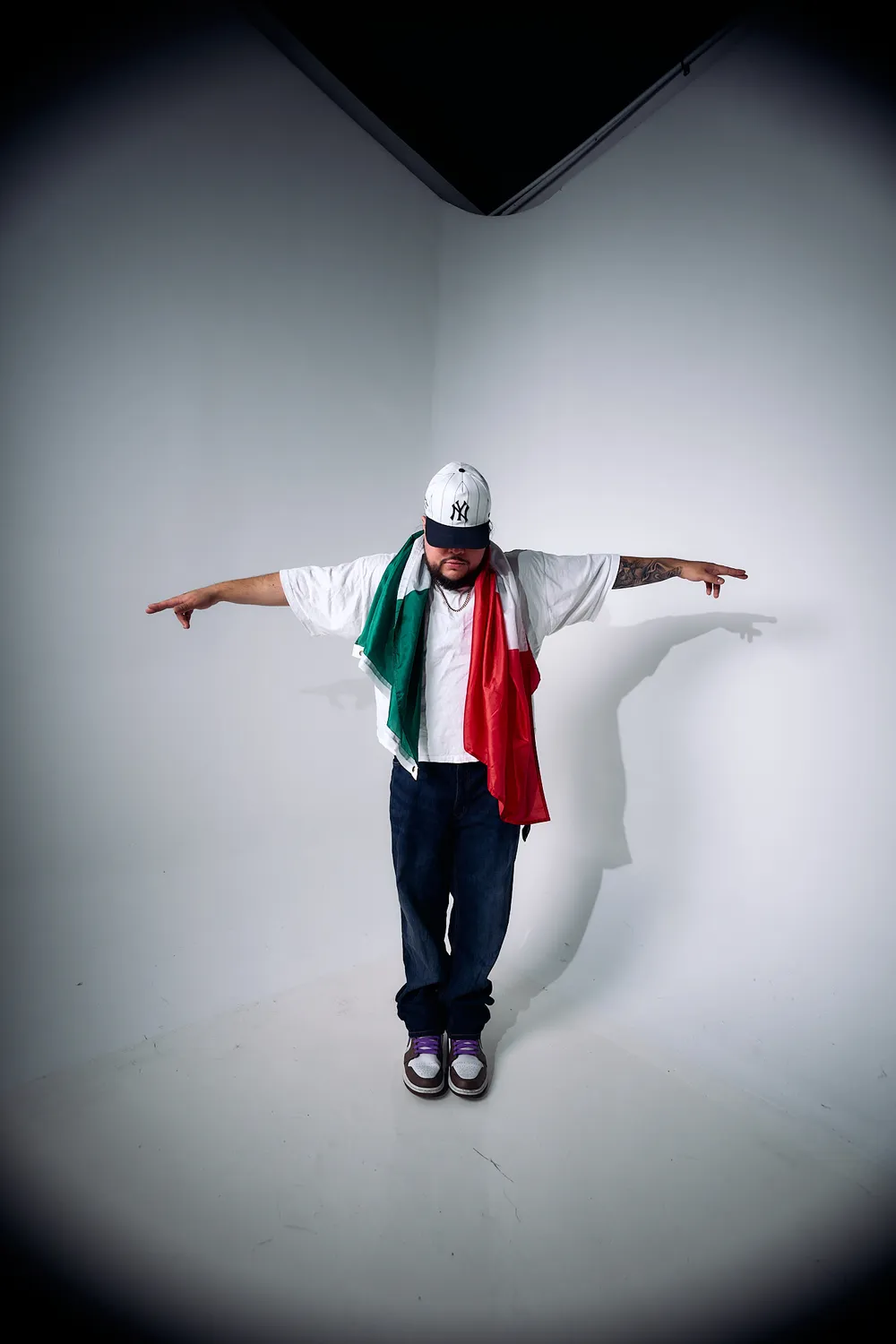 Papi AQ with arms spread, the Mexican flag over his shoulders.
