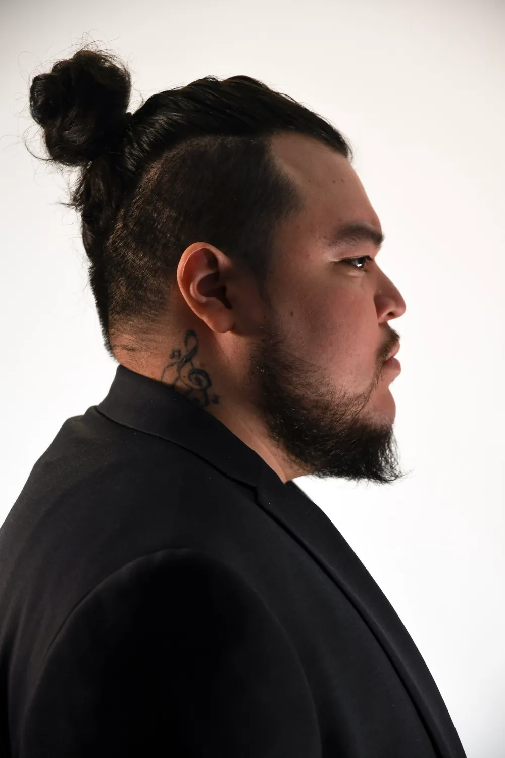 Papi AQ in profile, hair tied up, in a black jacket.