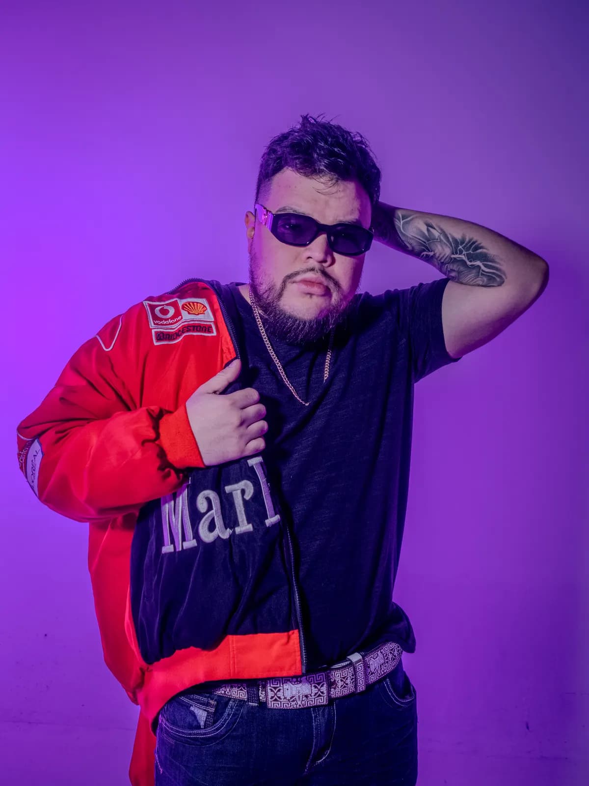 Papi AQ in sunglasses and a red racing jacket against purple light.