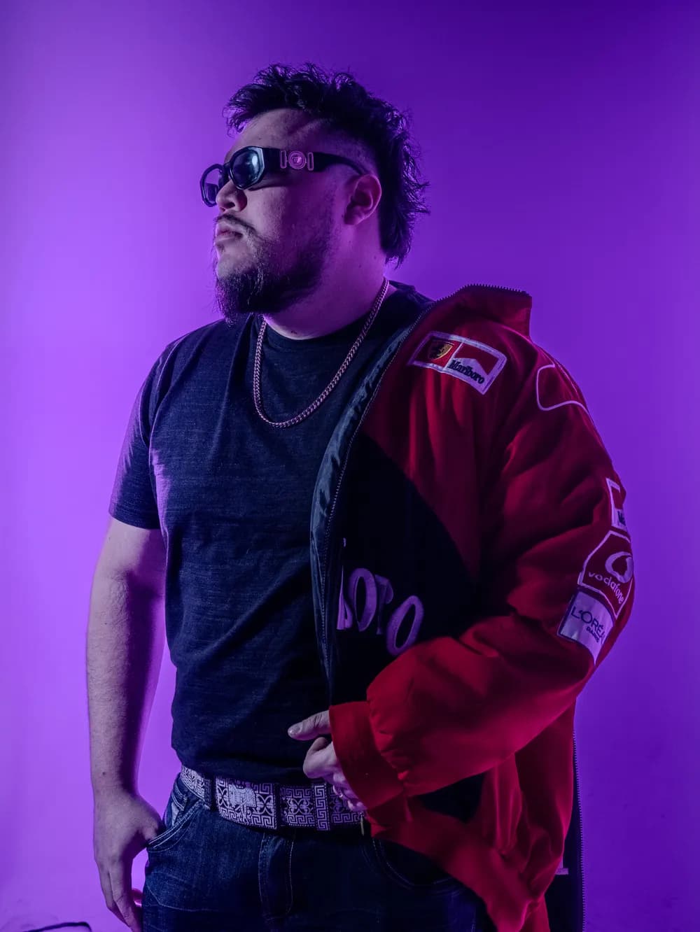 Papi AQ in a red racing jacket, looking up, in purple light.