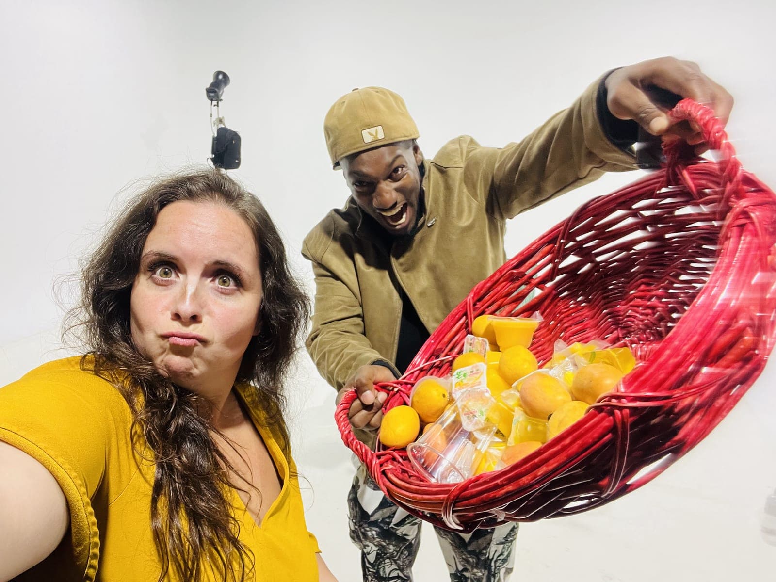 The same two guests pull faces, one pouting and one open mouthed, as the basket of mangoes tips toward the lens.