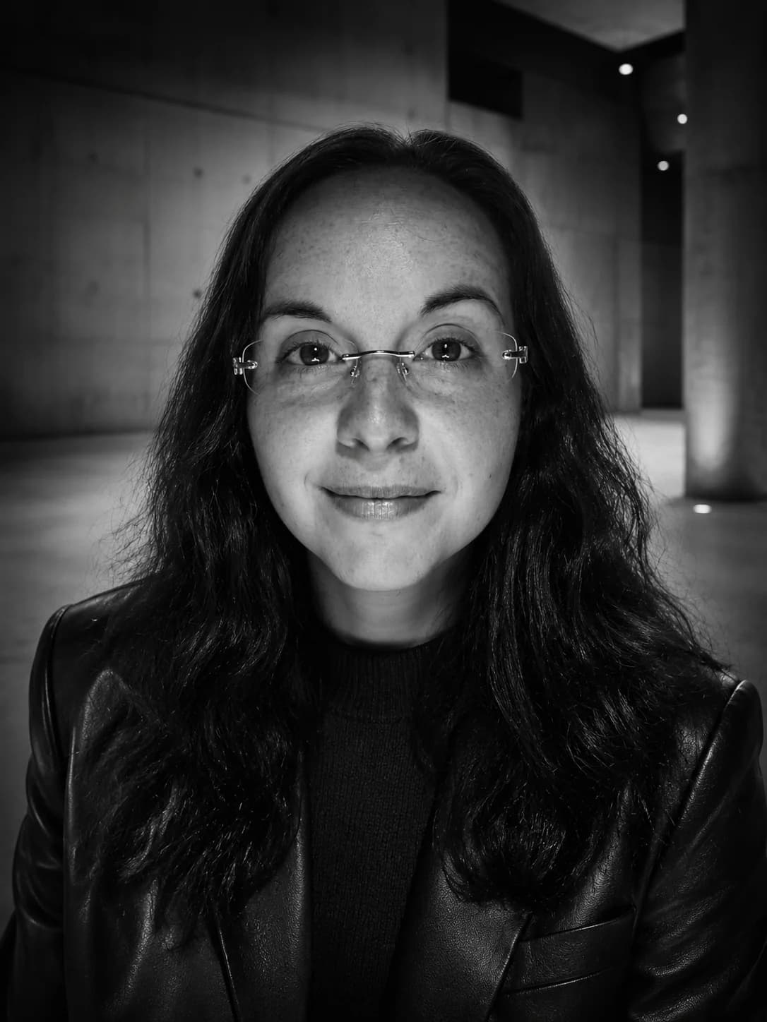 Amanda Andress in glasses and a leather jacket, photographed in black and white against a concrete wall.