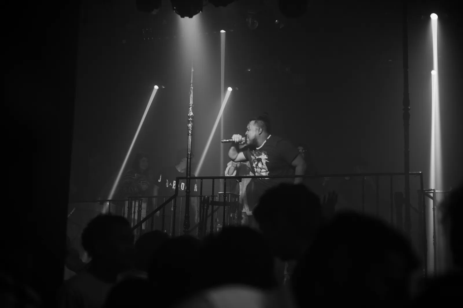 Papi AQ on stage under beams of light, the crowd in silhouette.